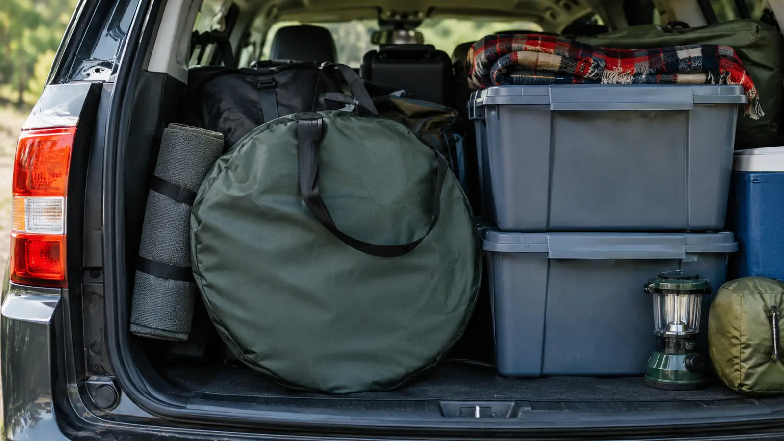 A round carry bag for a screen house packed flat beside plastic storage bins in the back of an SUV.