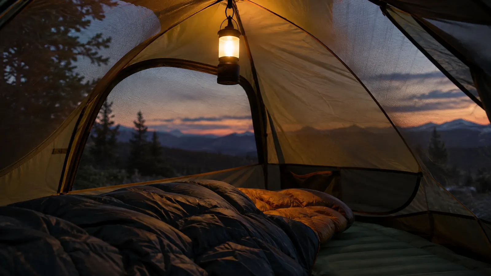 A lantern hanging from a loop inside a dome tent casting warm light over a sleeping bag