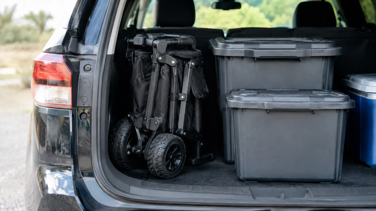 A folded wagon stowed in the back of an SUV beside plastic storage bins with the tailgate open